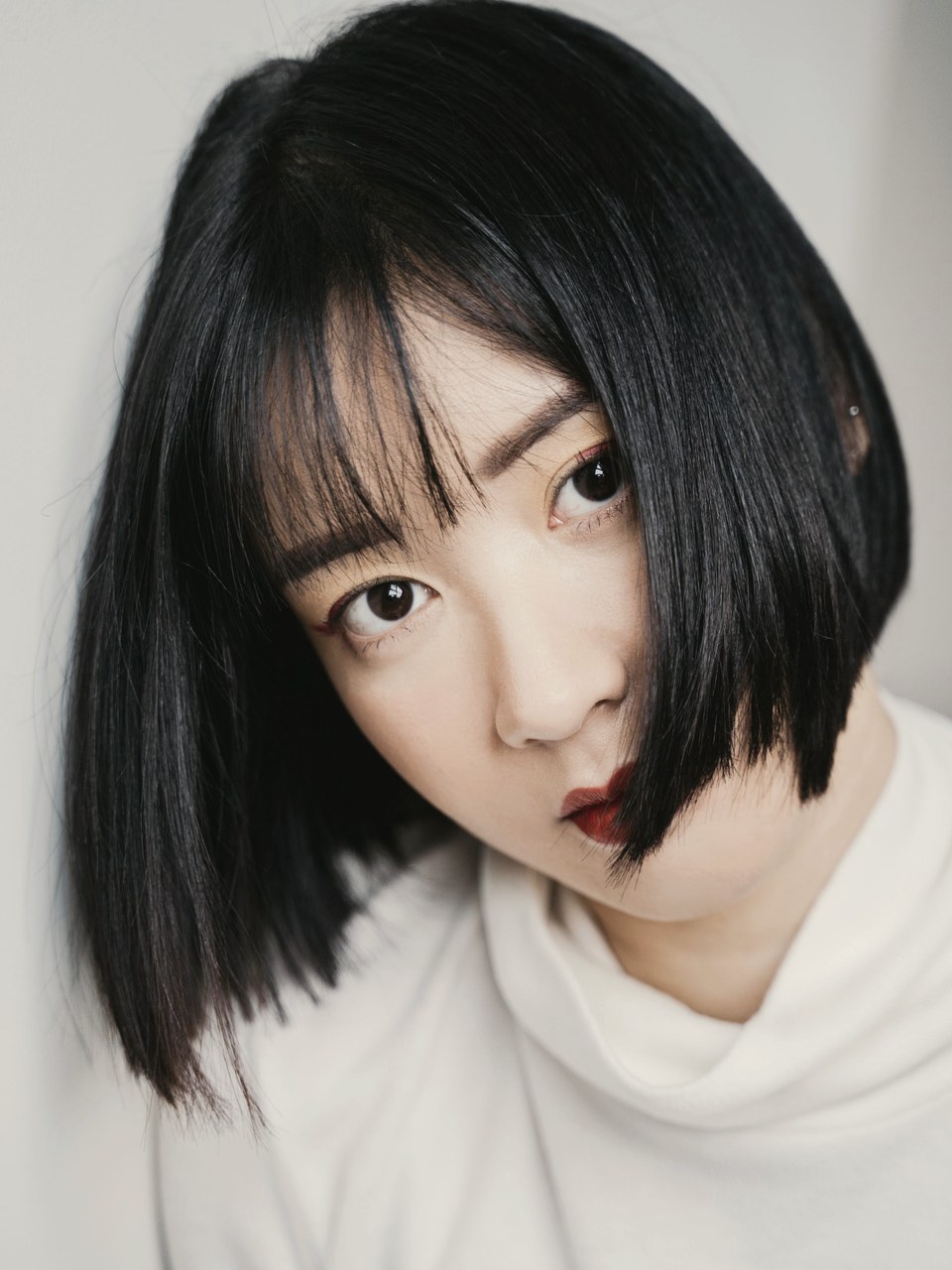 白いトップスを着て、毛先を内側へまとめた艶のある黒髪ボブの女性